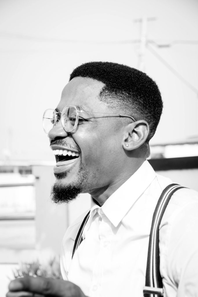 Black and white portrait of a joyful man in Accra, Ghana wearing stylish attire and glasses.